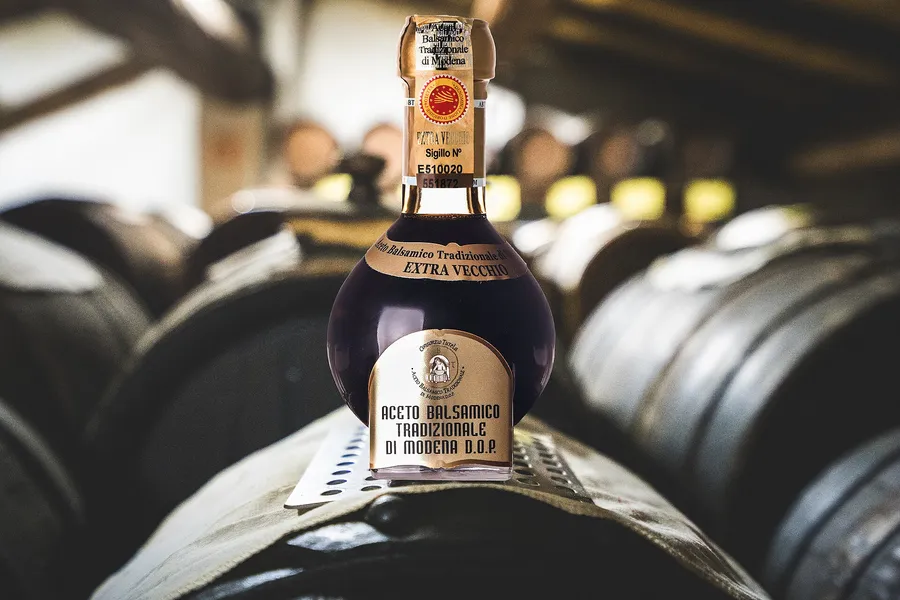 Una bottiglia di Aceto Balsamico Tradizionale di Modena DOP extravecchio appoggiata su una botte, in un'acetaia