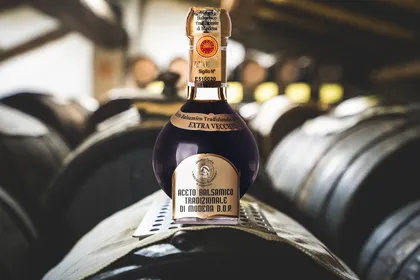 Una bottiglia di Aceto Balsamico Tradizionale di Modena DOP extravecchio appoggiata su una botte, in un'acetaia