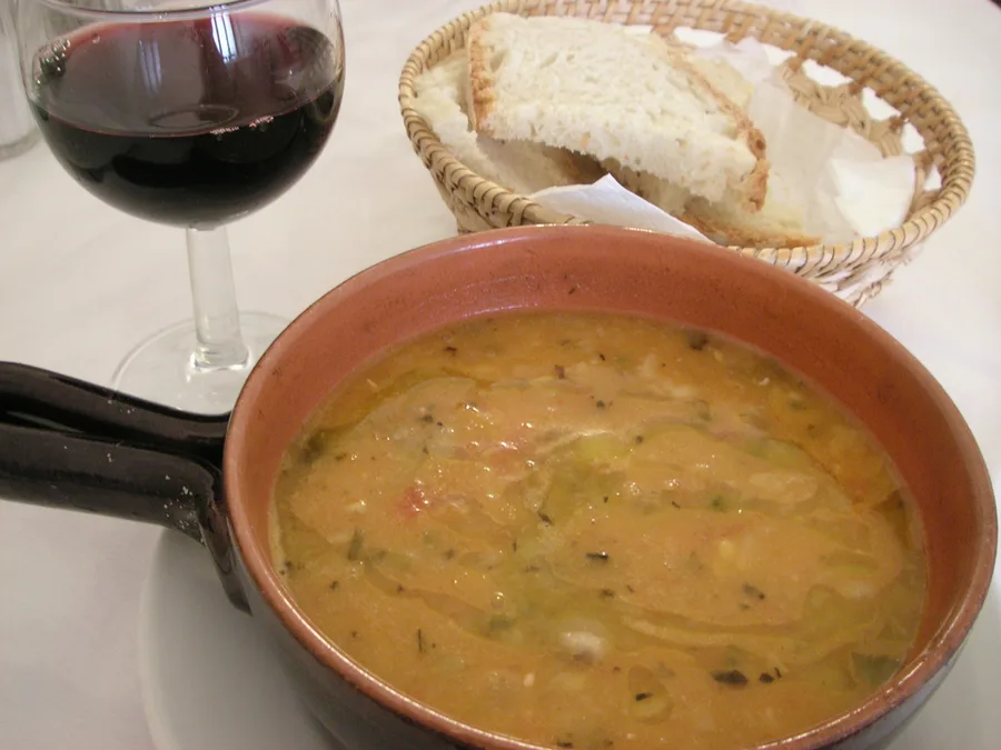 Zuppa di pane e verdure servita in una ciotola di coccio, con un bicchiere di vino rosso accanto